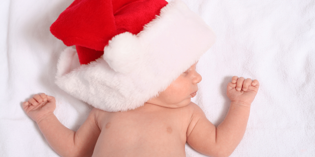 Baby, wearing a red and white Santa hat, asleep on white rug
